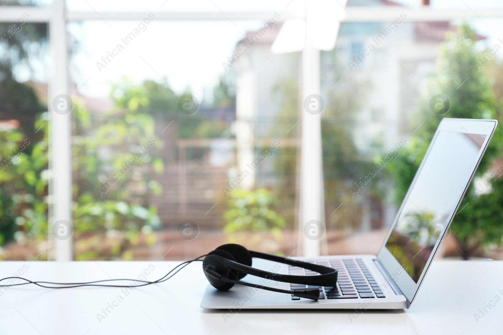 Photo of Modern laptop and headset on table indoors. Technical support concept