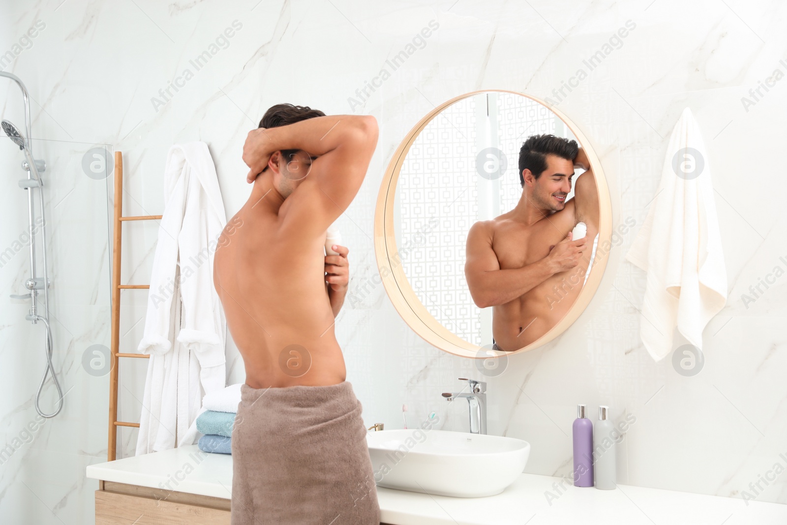 Photo of Handsome young man applying deodorant in bathroom