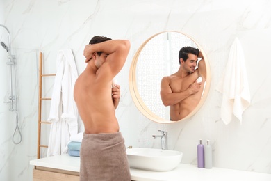 Photo of Handsome young man applying deodorant in bathroom