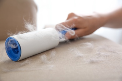 Woman removing hair from beige sofa, closeup