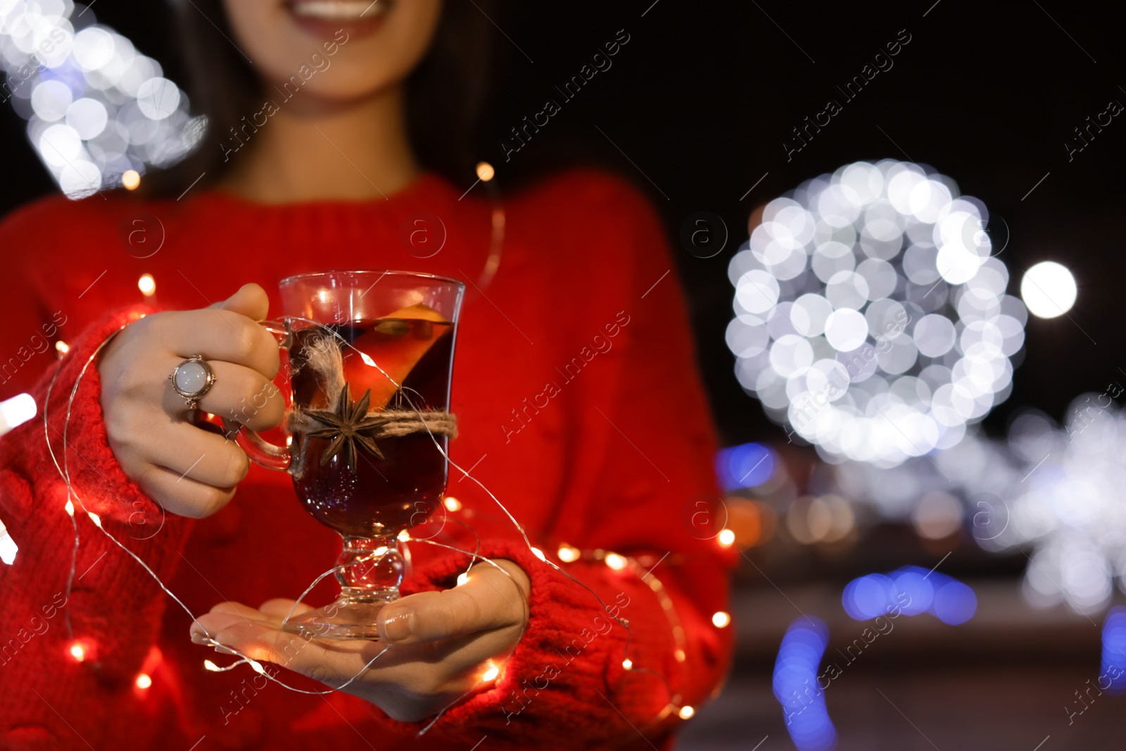 Photo of Woman with glass cup of mulled wine and garland at winter fair, closeup. Space for text