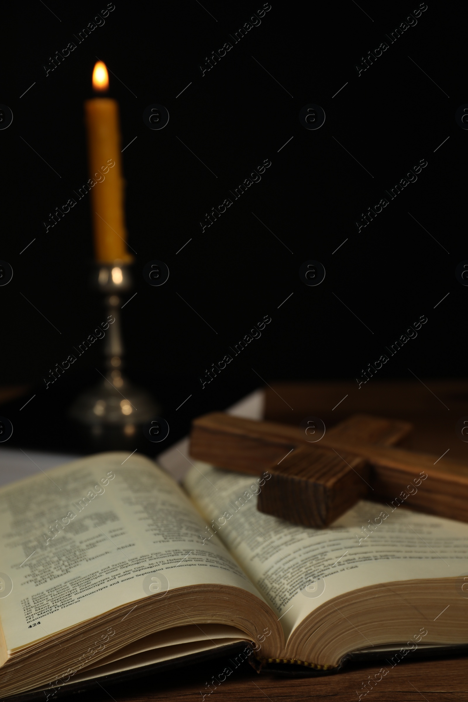 Photo of Church candle, Bible and cross on wooden table against black background