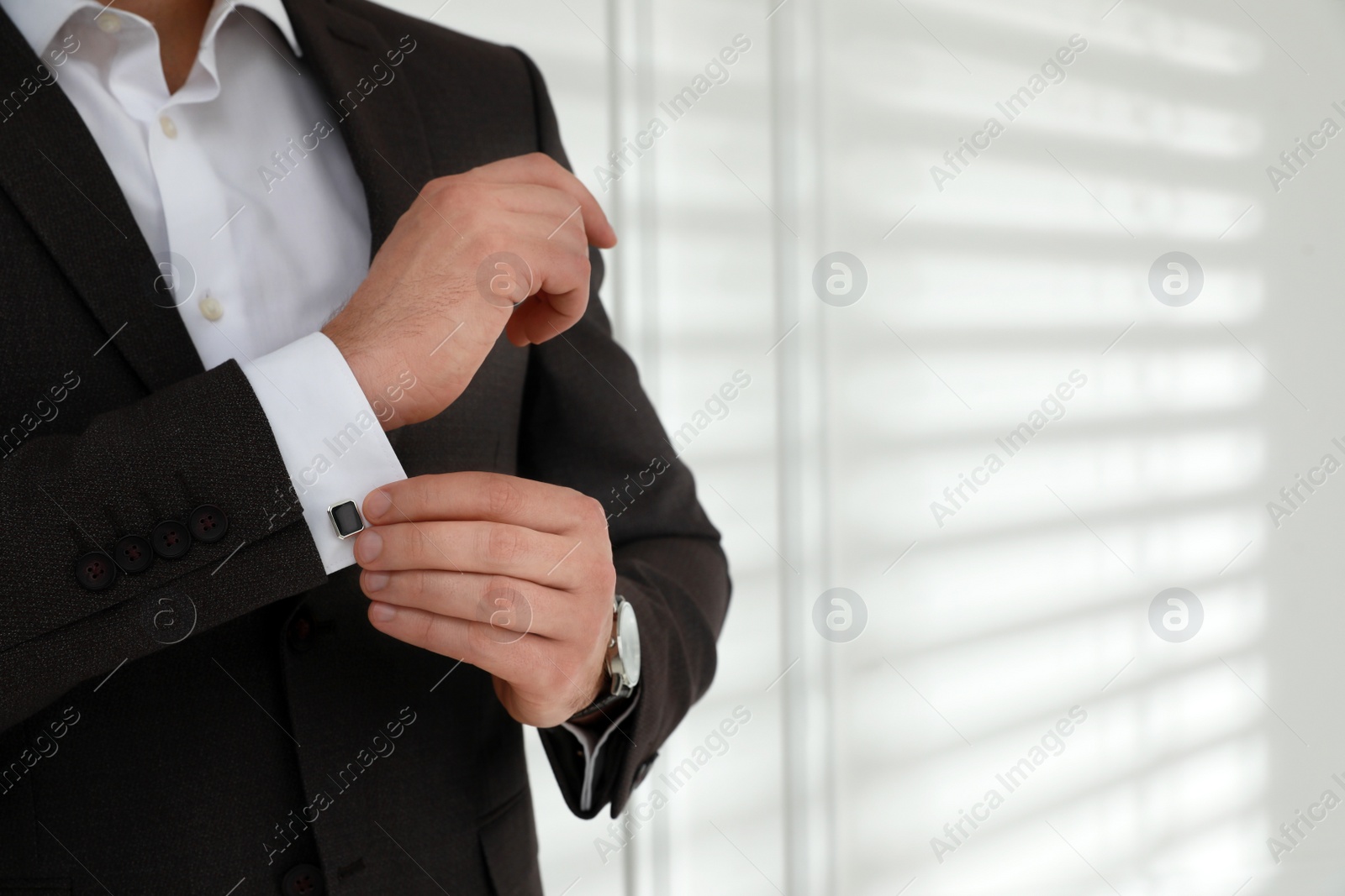 Photo of Man wearing stylish suit and cufflinks near white wall, closeup. Space for text