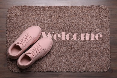 Image of Door mat with word WELCOME and shoes on wooden floor, top view