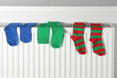 Different colorful socks hanging on white radiator indoors