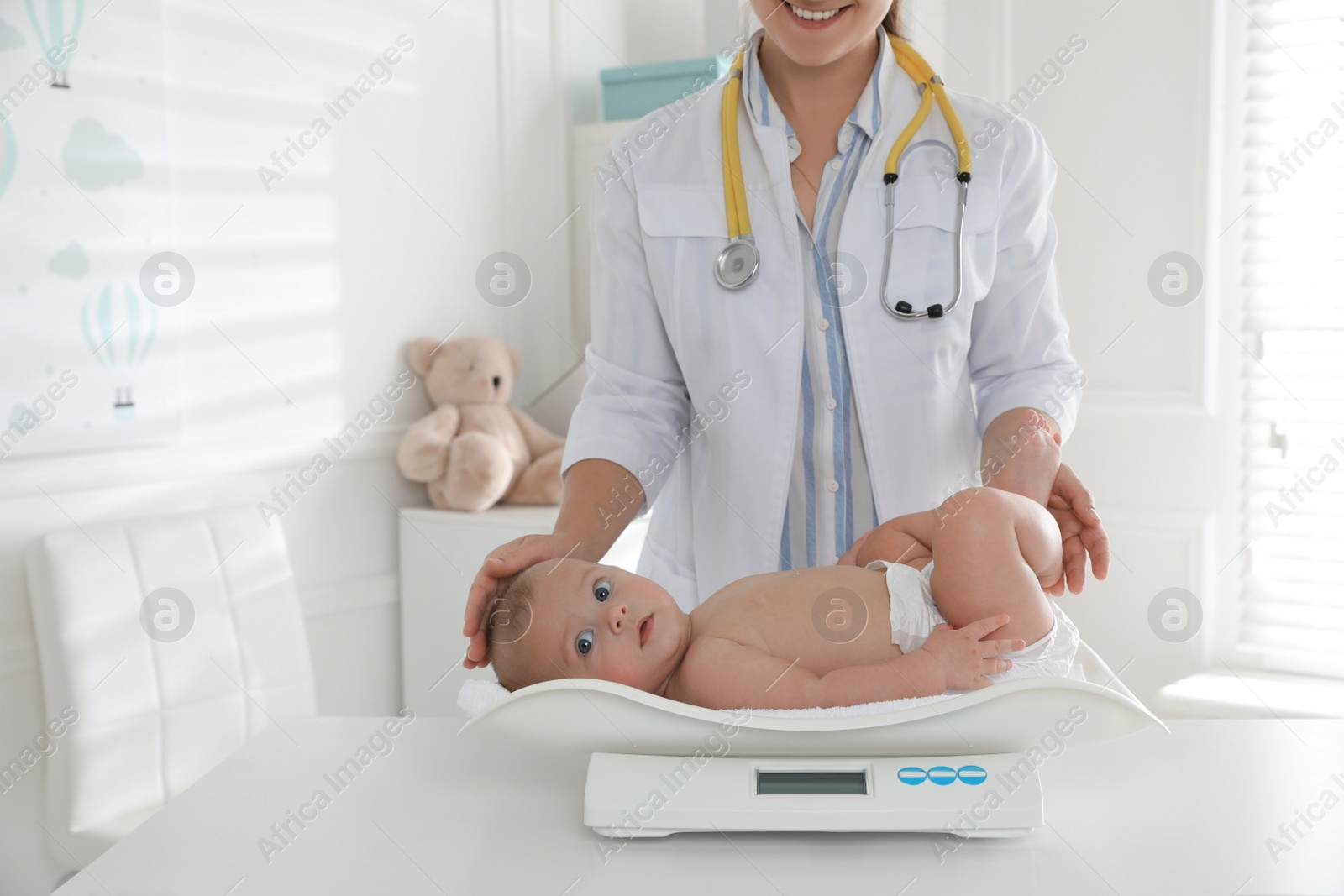 Photo of Pediatrician weighting cute baby in clinic, closeup. Health care