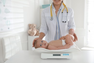 Pediatrician weighting cute baby in clinic, closeup. Health care