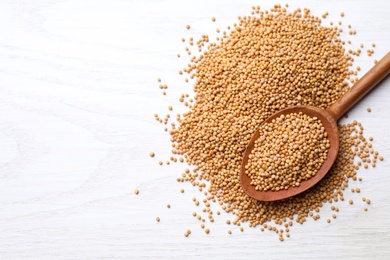 Photo of Mustard seeds with wooden spoon on white table, top view. Space for text