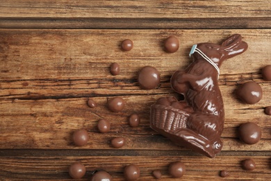 Photo of Chocolate bunny with protective mask, candies and space for text on wooden table, flat lay. Easter holiday during COVID-19 quarantine