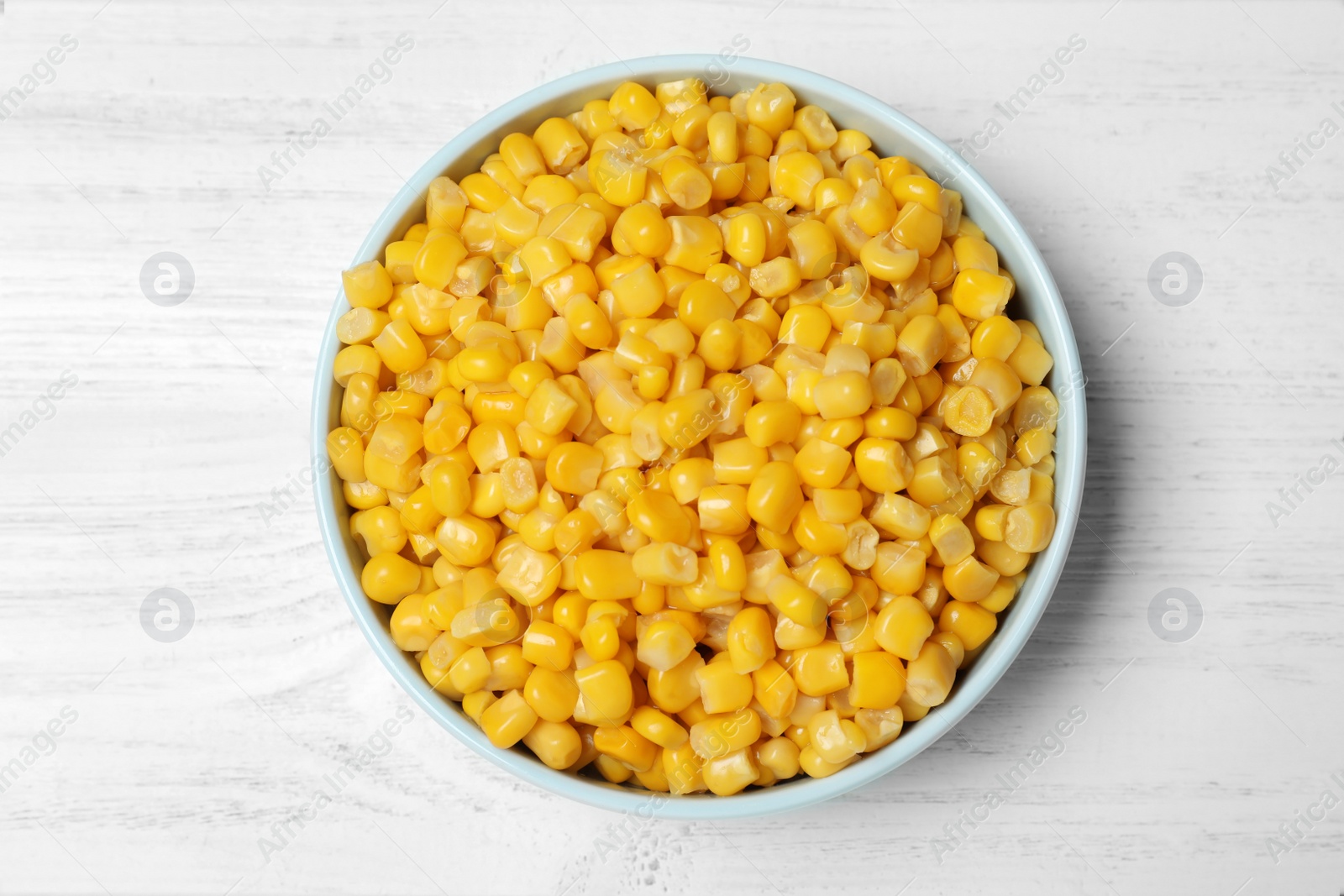 Photo of Delicious canned corn in bowl on white wooden table, top view