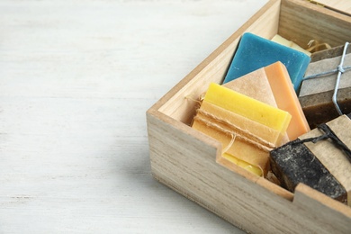 Photo of Different handmade soap bars in wooden box on table, closeup. Space for text