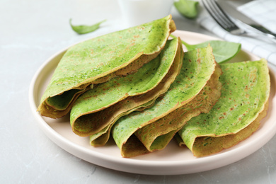 Tasty spinach crepes on light grey table, closeup