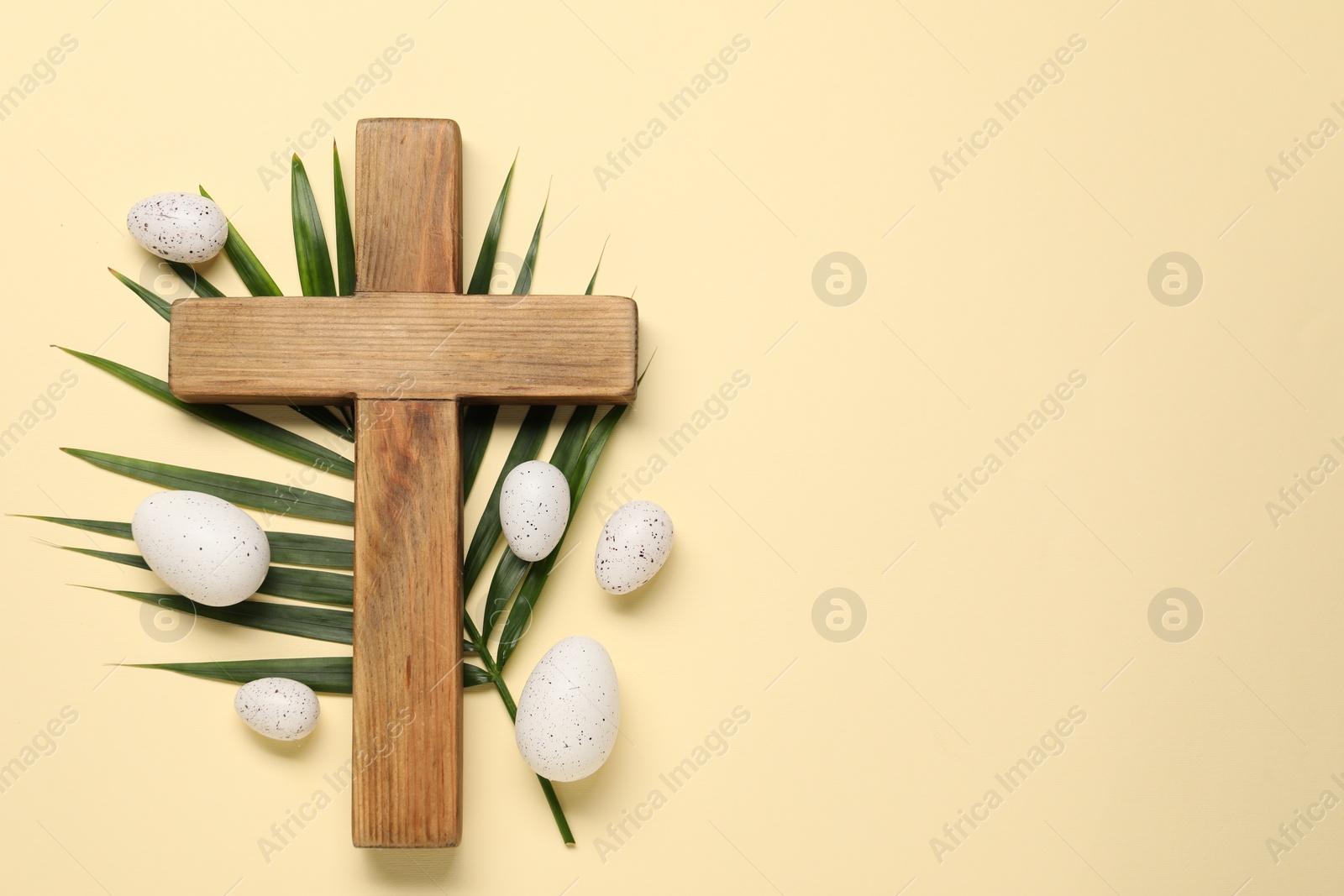 Photo of Wooden cross, painted Easter eggs and palm leaf on beige background, flat lay. Space for text