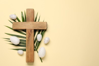 Photo of Wooden cross, painted Easter eggs and palm leaf on beige background, flat lay. Space for text