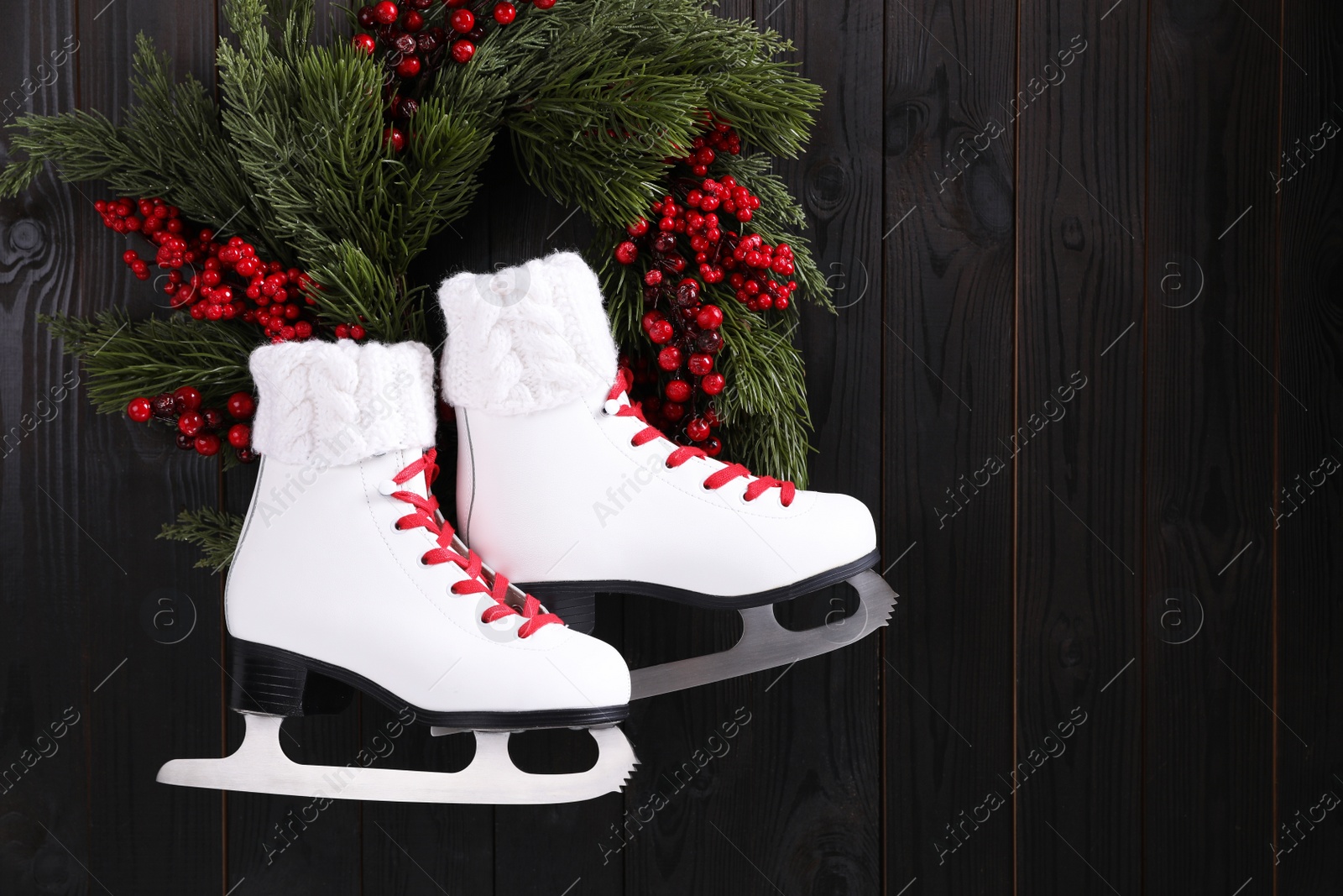 Photo of Pair of ice skates and beautiful Christmas wreath hanging on dark wooden wall, space for text