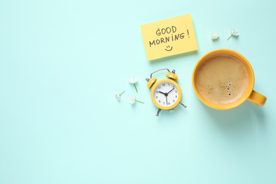 Photo of Delicious coffee, alarm clock and card with GOOD MORNING wish on light blue background, flat lay. Space for text