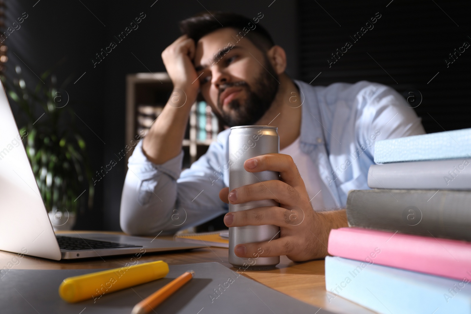 Photo of Tired young man with energy drink studying at home, focus on hand