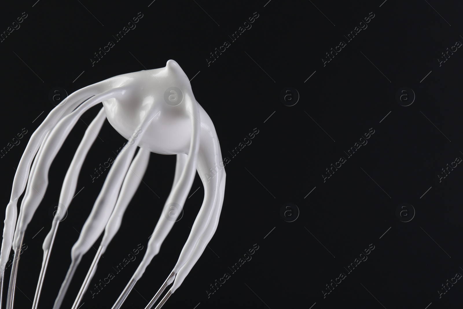 Photo of Whisk with whipped cream on black background, closeup. Space for text