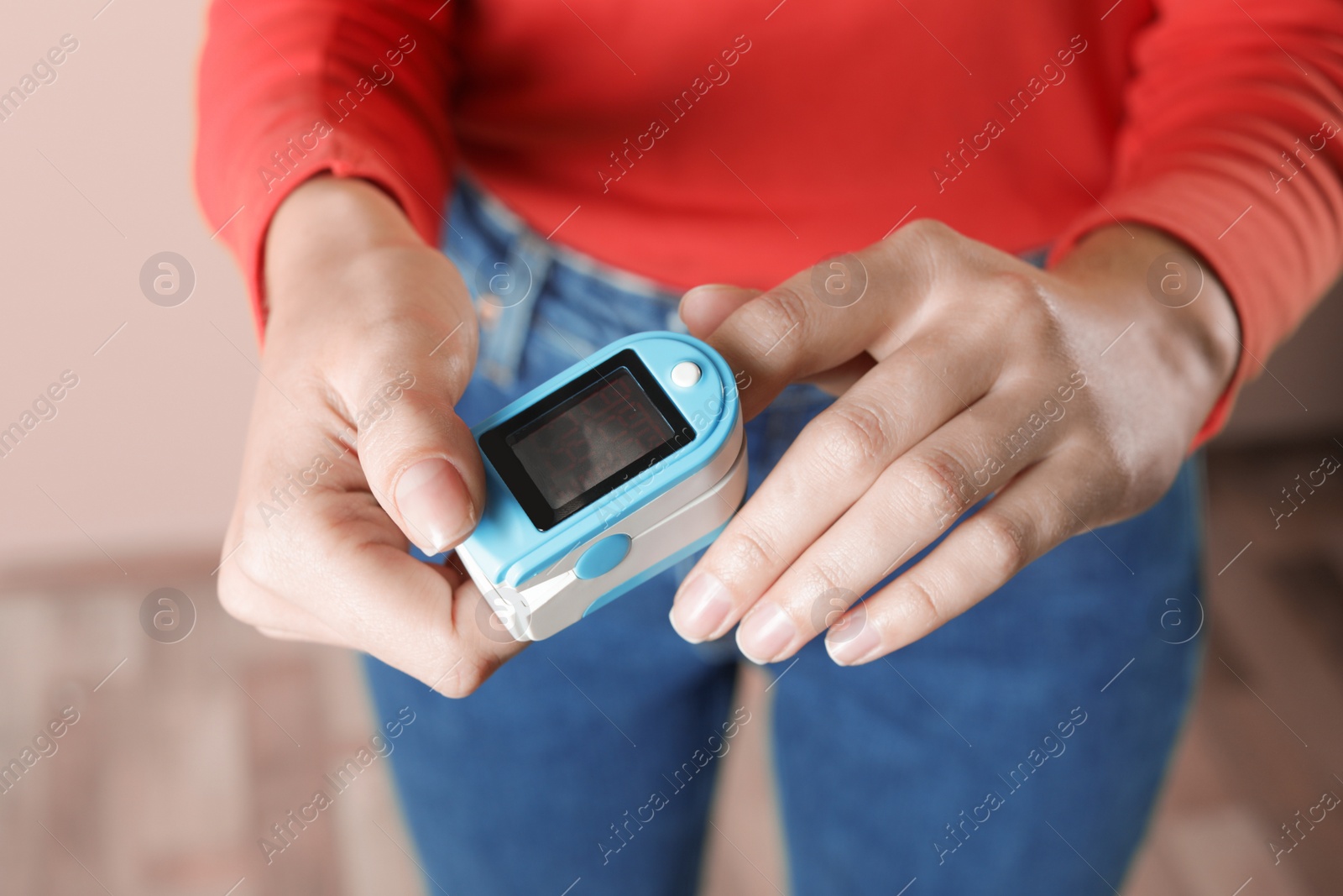 Photo of Young woman checking pulse with digital medical device indoors, closeup