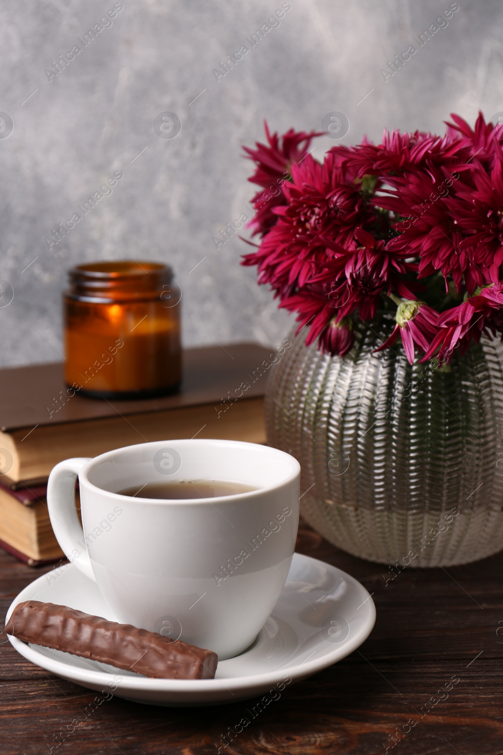 Photo of Beautiful pink chrysanthemum flowers and cup of aromatic tea with sweet chocolate cookie on wooden table