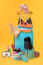 Photo of Suitcase, clothes and beach accessories on yellow background. Summer vacation