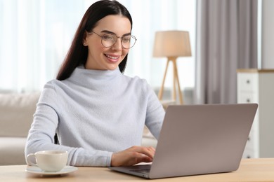 Photo of Happy woman working with laptop at wooden desk in room