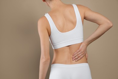 Photo of Woman suffering from pain in back on beige background, closeup