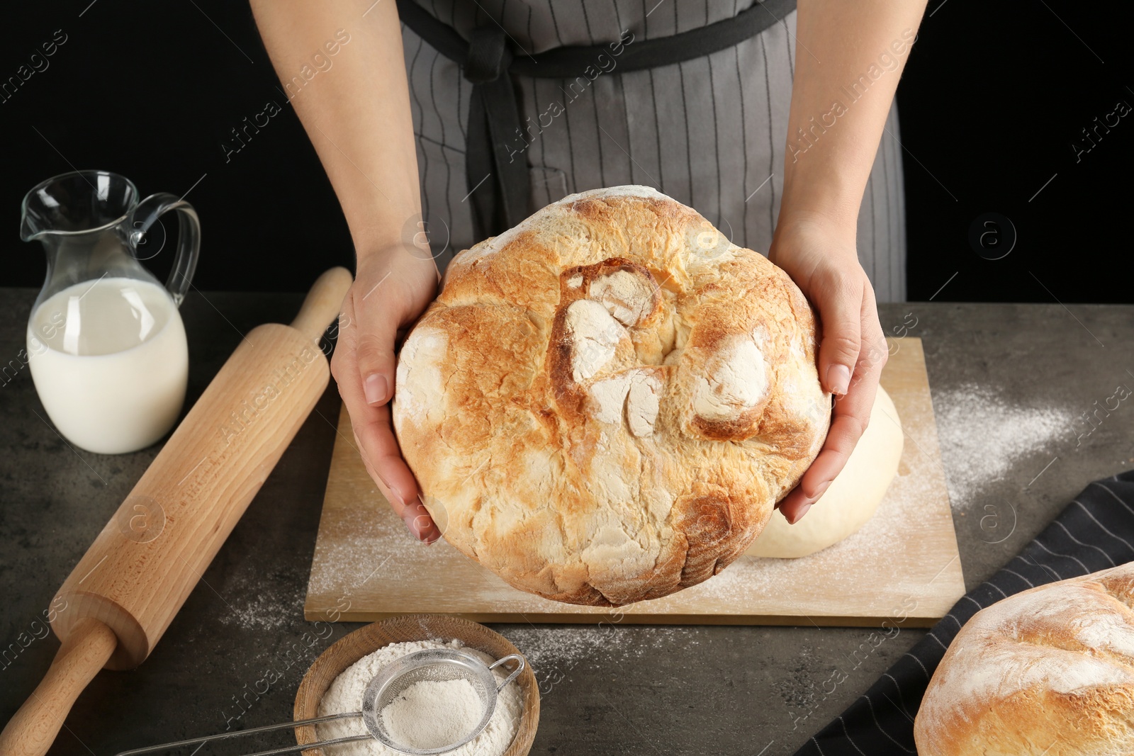 Photo of Female baker holding loaf of bread over kitchen table, closeup