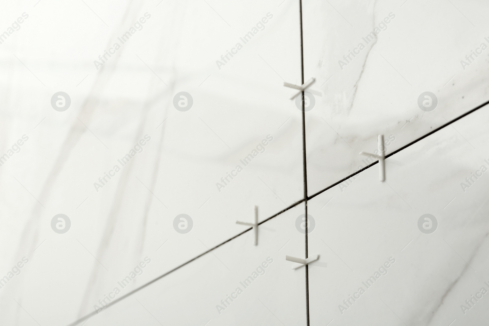 Photo of Closeup view of ceramic tiles with plastic crosses in joints on wall. Building and renovation works