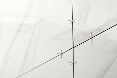 Photo of Closeup view of ceramic tiles with plastic crosses in joints on wall. Building and renovation works