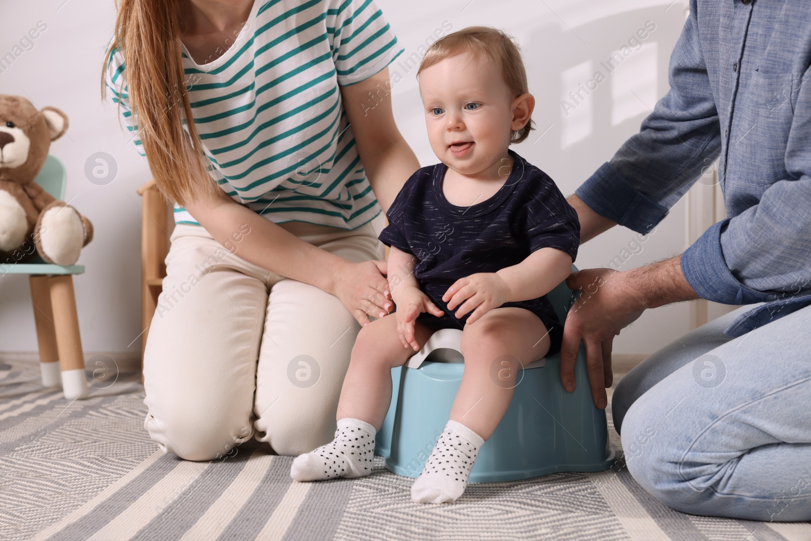 Photo of Parents training their child to sit on baby potty indoors