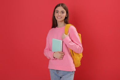 Photo of Teenage student with backpack and book on red background