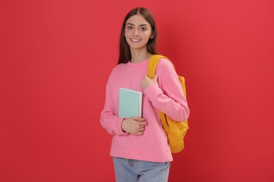 Teenage student with backpack and book on red background