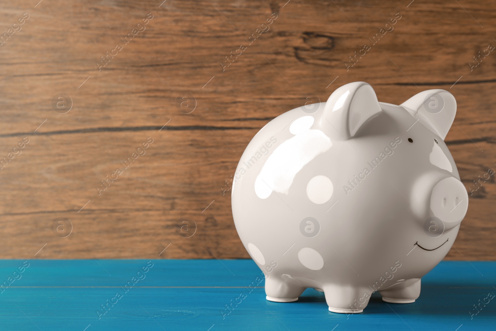 Photo of Ceramic piggy bank on blue wooden table. Space for text