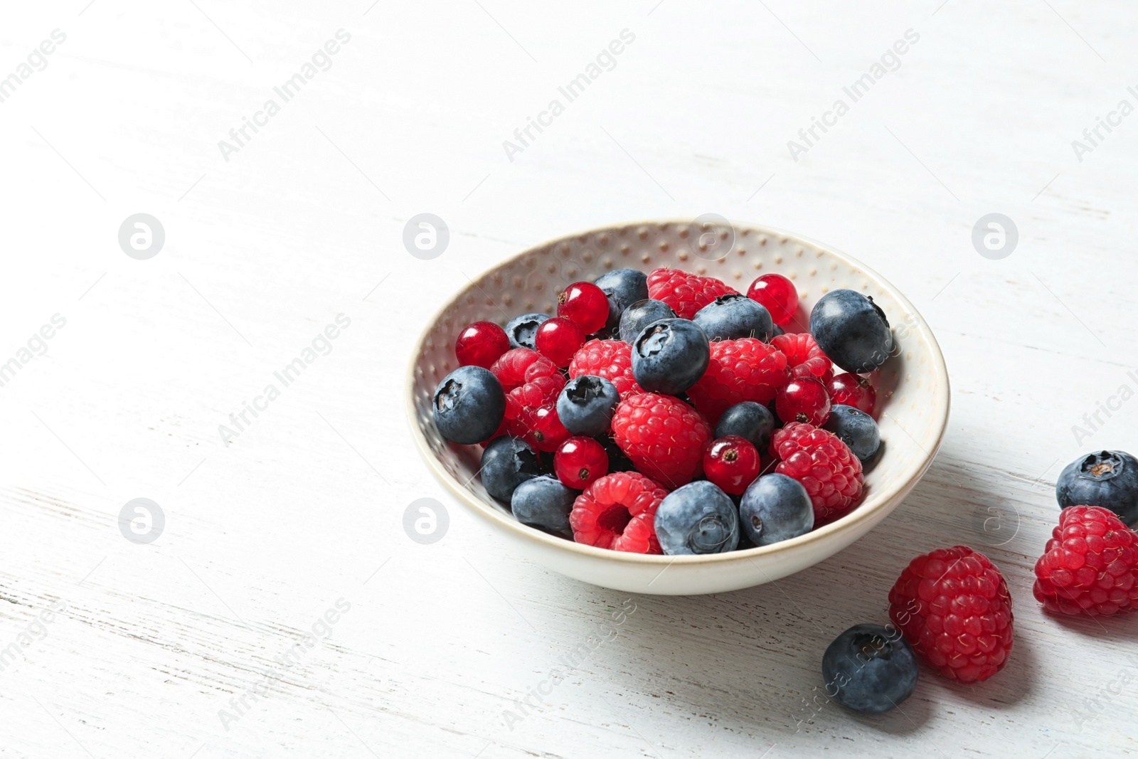 Photo of Bowl with raspberries, red currant and blueberries on wooden table