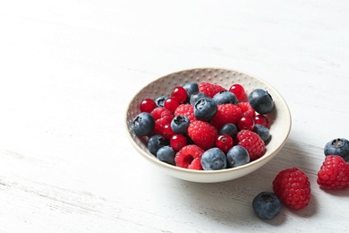 Photo of Bowl with raspberries, red currant and blueberries on wooden table