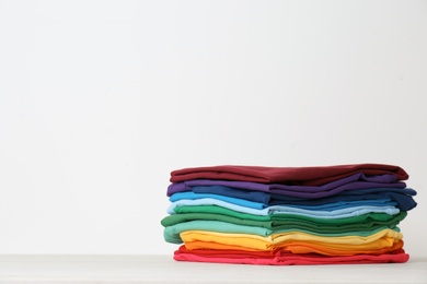 Stack of bright folded clothes on table against white background. Space for text