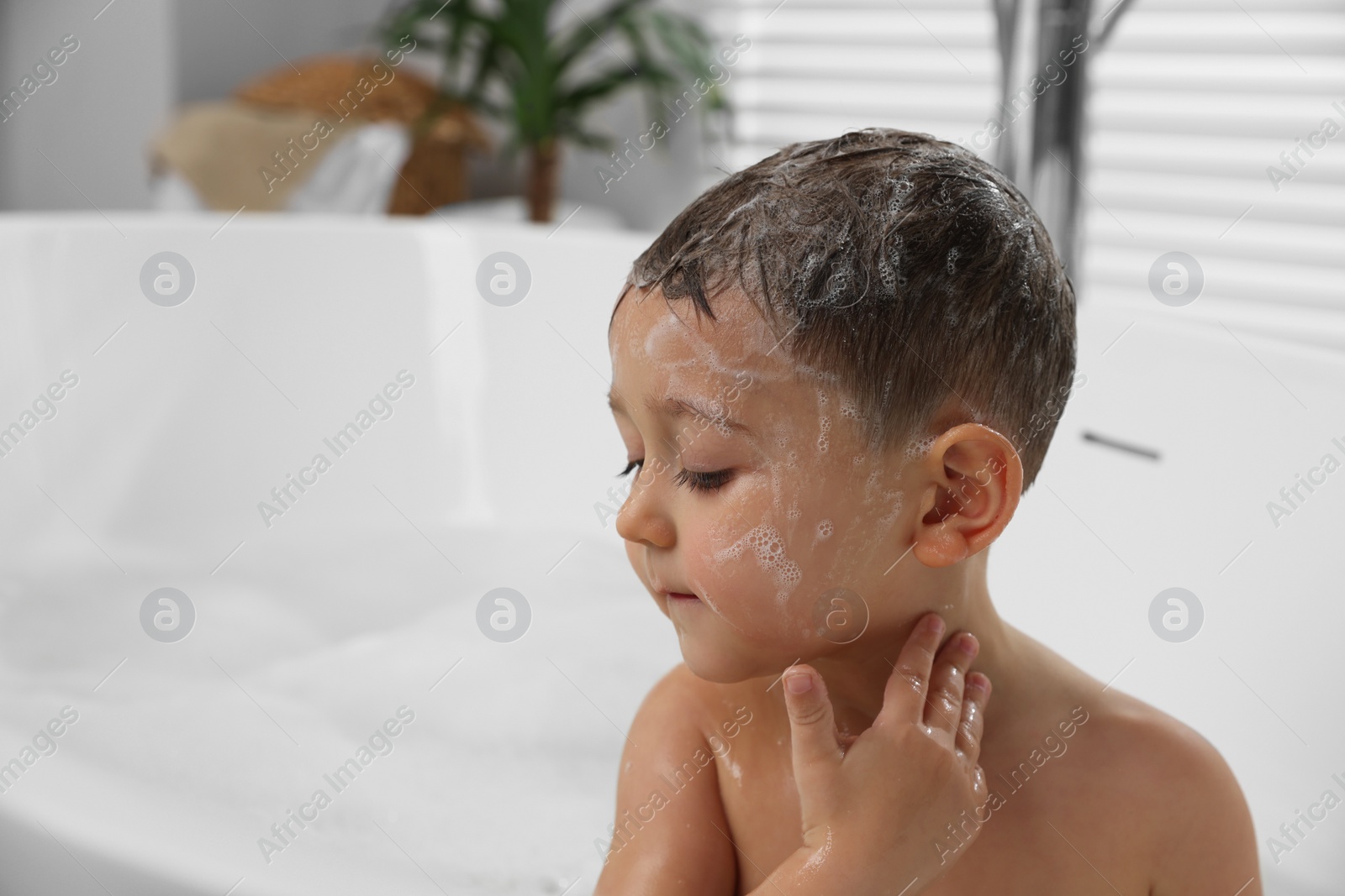 Photo of Cute little boy washing hair with shampoo in bathroom. Space for text