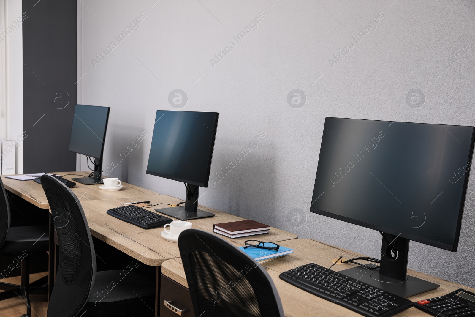 Photo of Open office interior. Modern workplaces with computers near light grey wall