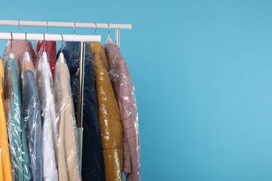 Photo of Dry-cleaning service. Many different clothes in plastic bags hanging on rack against light blue background, space for text