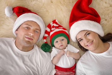 Photo of Happy couple with baby in Christmas hats on fuzzy rug, top view