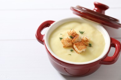 Photo of Tasty potato soup with croutons and rosemary in ceramic pot on white wooden table. Space for text