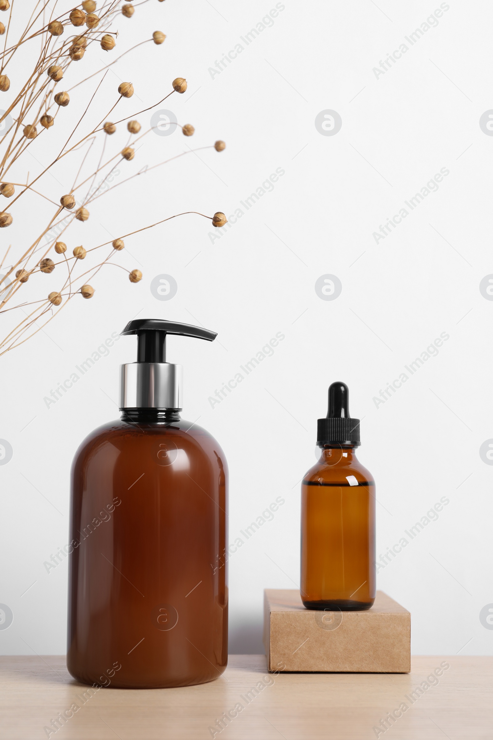 Photo of Bottles of cosmetic products and dry spikes on wooden table