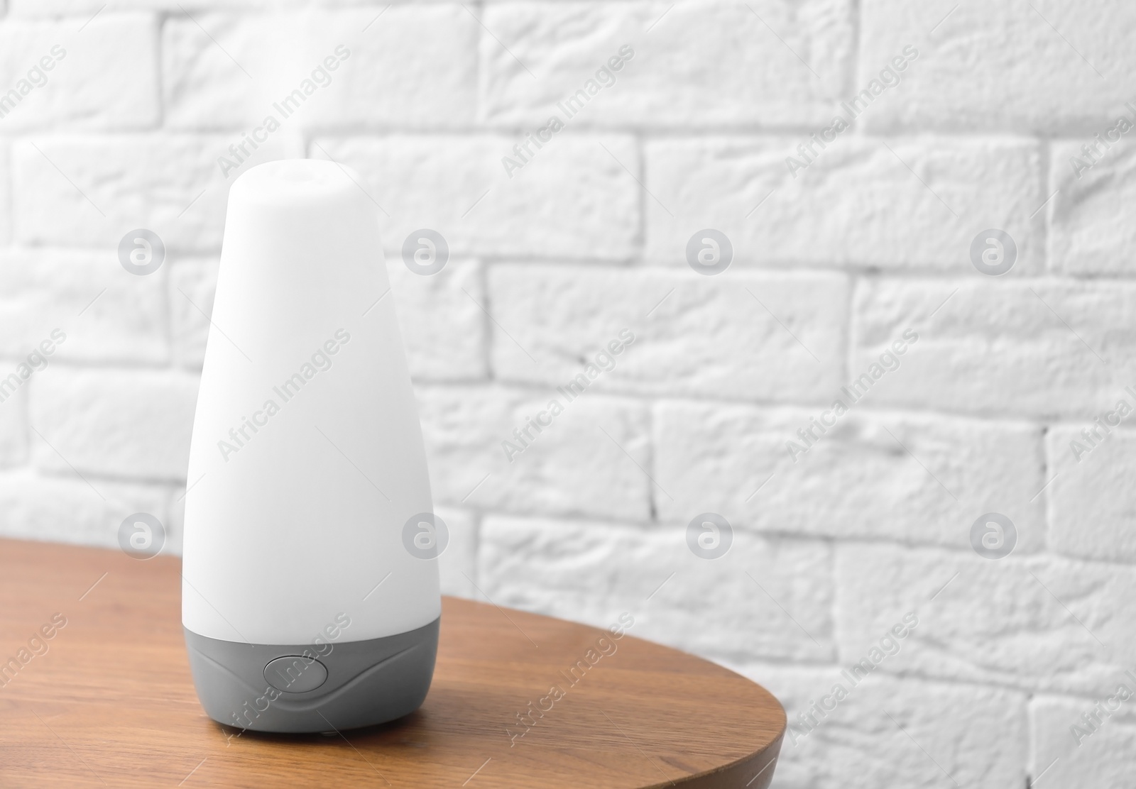 Photo of Essential oils diffuser on wooden table near brick wall. Space for text