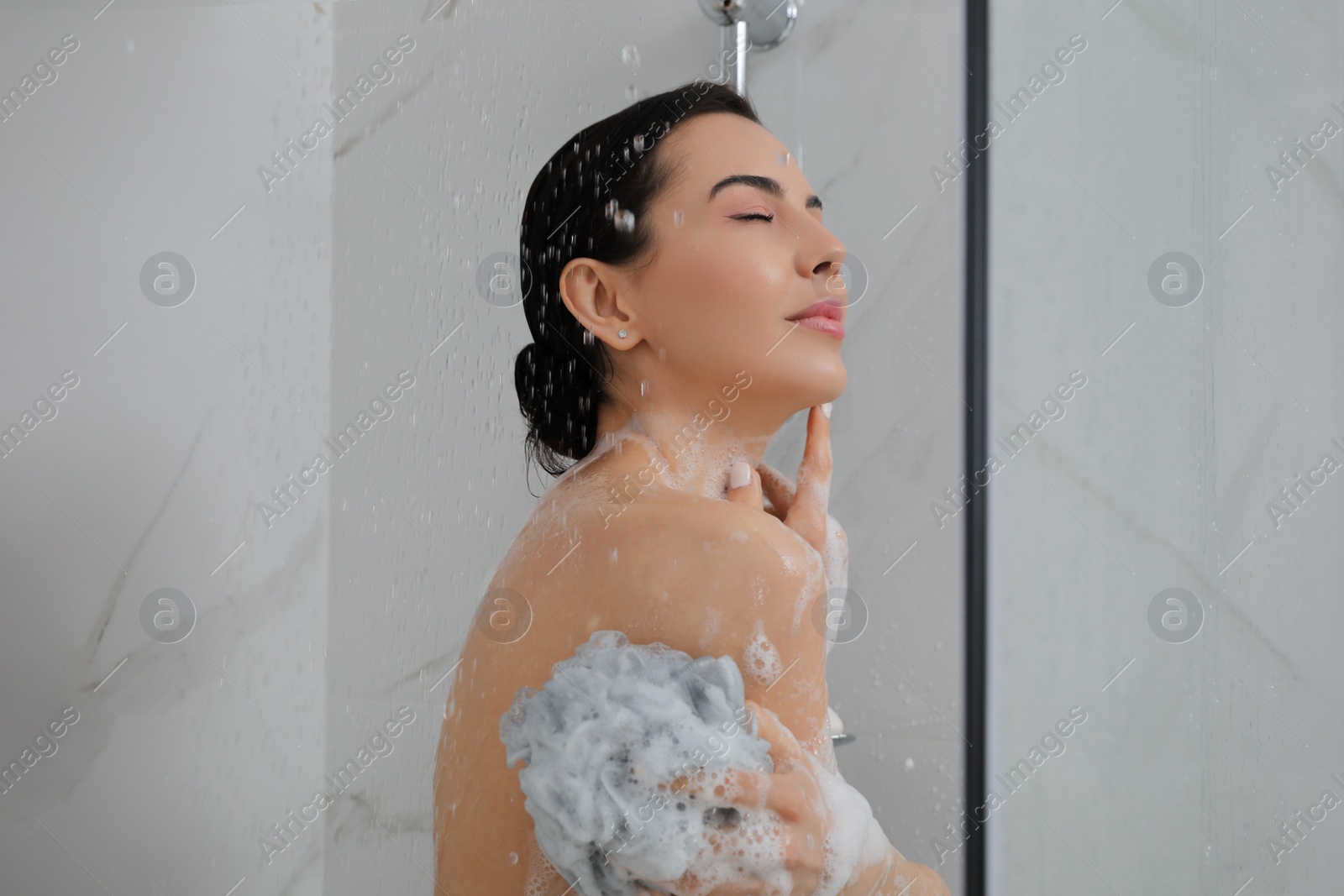 Photo of Young woman with mesh pouf taking shower at home