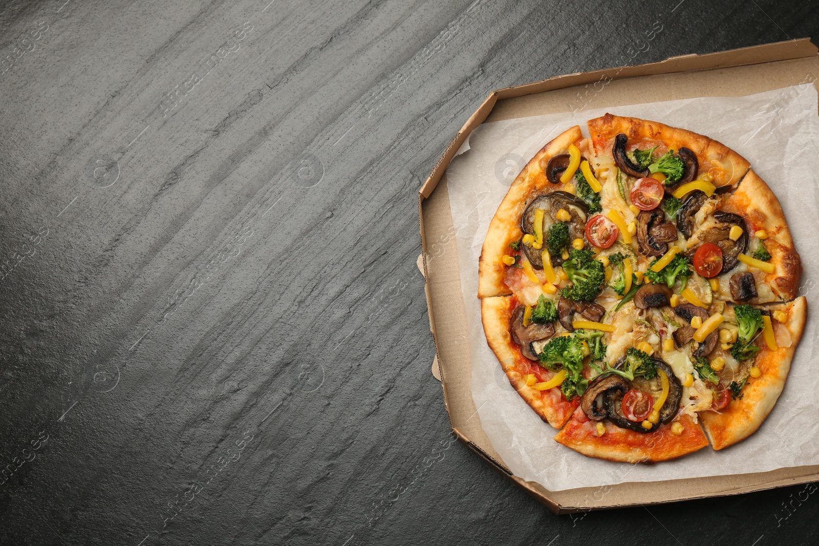 Photo of Delicious vegetarian pizza with mushrooms, cheese and vegetables in box on black table, top view. Space for text