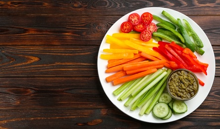 Celery and other vegetable sticks with dip sauce on wooden table, top view. Space for text
