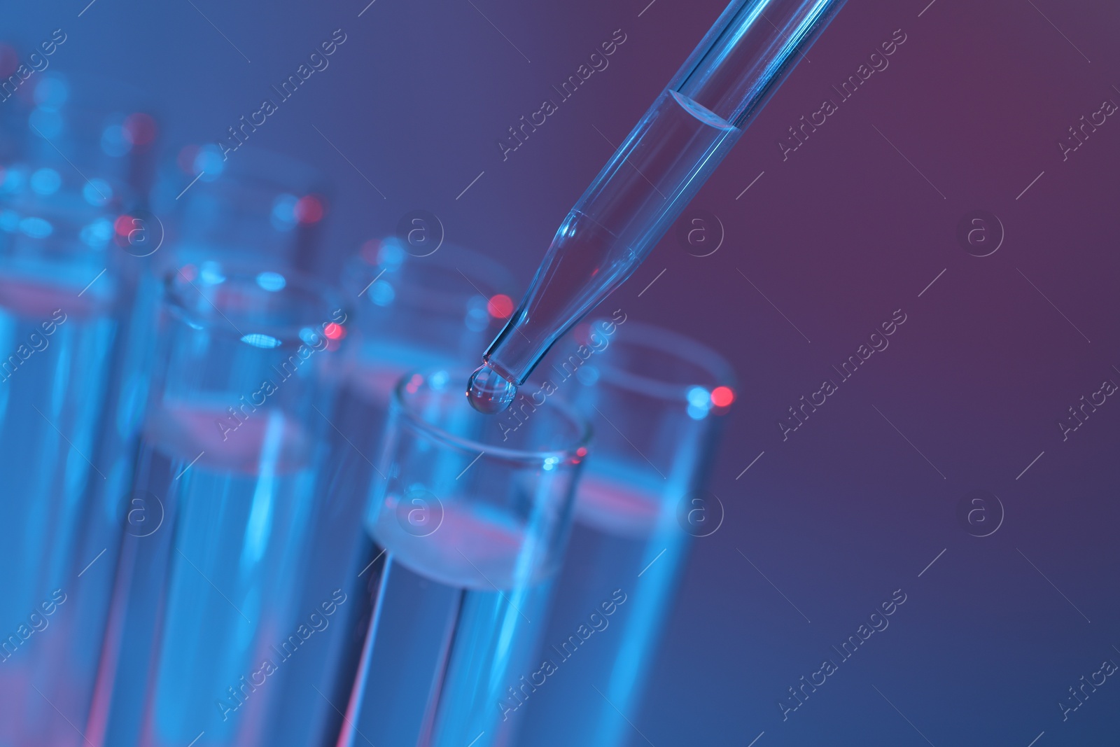 Photo of Dripping liquid from pipette into test tube on color background, closeup