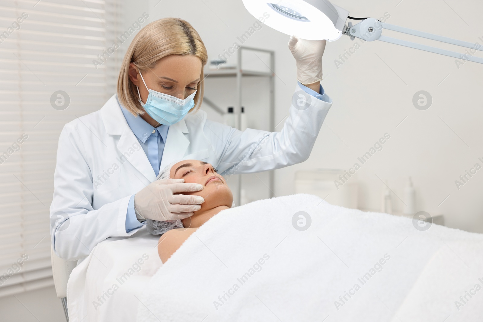 Photo of Dermatologist examining patient`s face under lamp in clinic