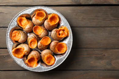 Delicious cooked snails on wooden table, top view. Space for text